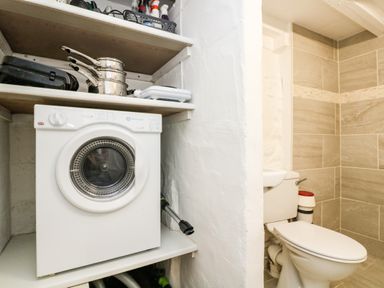 A white washing machine on a shelf next to a toilet with tiled walls at The Old Stable in Porthallow