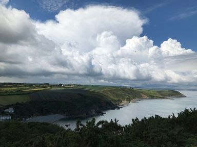 A coastal landscape with cliffs green fields and large clouds over the sea at The Old Stable in Porthallow