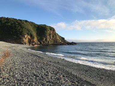 A pebble beach with waves and a green hill under a blue sky at The Old Stable in Porthallow