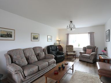 A living room with patterned sofas and armchairs a wooden coffee table and framed pictures on the wall at Bryn Afon Farm in Llanrug