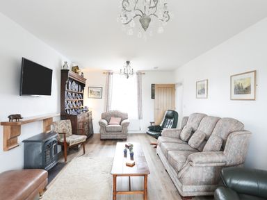 A living room with sofas a television mounted on the wall and a wooden cabinet displaying blue and white plates at Bryn Afon Farm in Llanrug