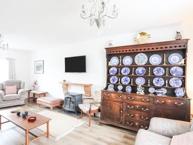 A living room with a wooden cabinet displaying blue and white plates and brass candlesticks at Bryn Afon Farm in Llanrug