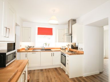 A kitchen with white cabinets wooden countertops a microwave and a red window blind at Bryn Afon Farm in Llanrug