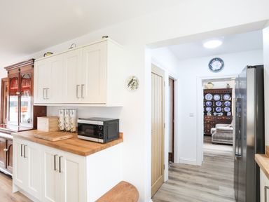 A kitchen with white cabinets wooden countertop a microwave and a wooden cabinet with glass doors at Bryn Afon Farm in Llanrug