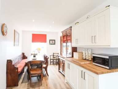 A kitchen dining area with wooden dining table and chairs a wooden cabinet white cupboards and a microwave at Bryn Afon Farm in Llanrug