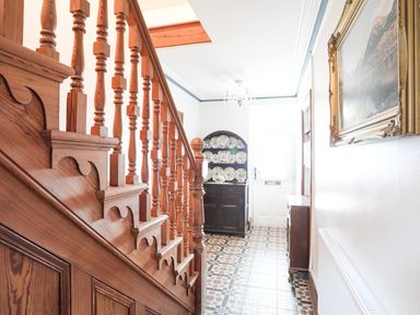 A hallway with wooden staircase and tiled floor with a cabinet displaying plates at Bryn Afon Farm in Llanrug