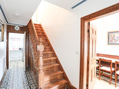 A hallway with wooden stairs and an open door leading to a dining area at Bryn Afon Farm in Llanrug