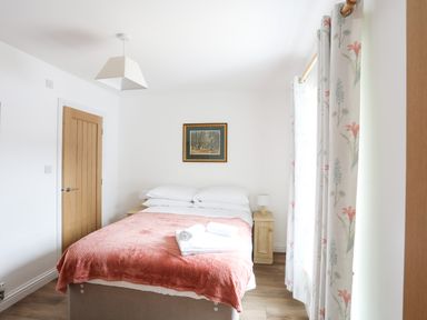 A bedroom with a bed covered with a pink blanket and white towels on top at Bryn Afon Farm in Llanrug