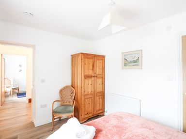 A bedroom with a wooden wardrobe a chair and a bed covered with a pink blanket at Bryn Afon Farm Llanrug