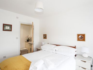 A bedroom with a bed yellow blanket white pillows and linens bedside tables with lamps and an open door leading to a bathroom at Bryn Afon Farm in Llanrug