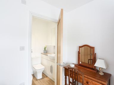 A wooden dressing table with a chair and lamp next to a door opening to a bathroom with a toilet and a sink at Bryn Afon Farm in Llanrug