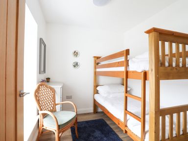 A bedroom with wooden bunk beds a wicker chair a small white chest of drawers and wall plates at Bryn Afon Farm in Llanrug