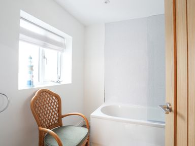 A bathroom with a wicker chair a bathtub a window with blinds and nautical decorations at Bryn Afon Farm Llanrug