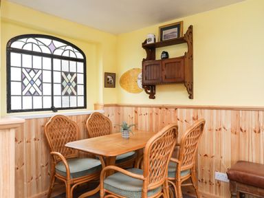 A dining area with a wooden table and four chairs near a stained glass window and a wall cabinet at Bryn Afon Farm in Llanrug