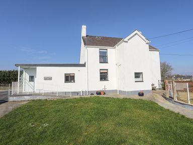 A white two-story house with a sloped roof and grass in front at Bryn Afon Farm in Llanrug
