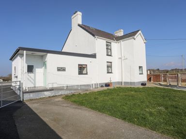 A white two-story house with a green door and railing next to a grassy area at Bryn Afon Farm in Llanrug