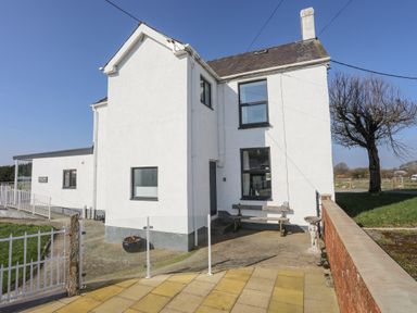 An exterior view of a white two-story house with a bench and tree next to it at Bryn Afon Farm in Llanrug