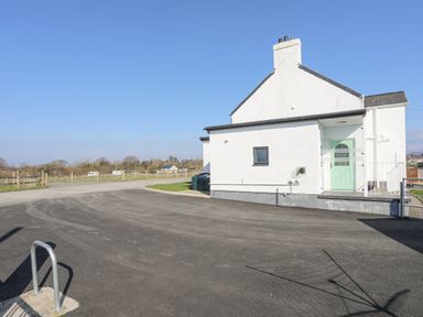 The exterior of a white house with a mint green door next to a paved driveway and a fenced field at Bryn Afon Farm in Llanrug