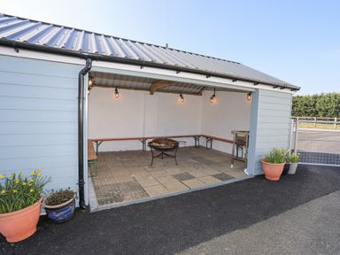 An open outdoor seating area with benches, a fire pit, and potted plants at Bryn Afon Farm in Llanrug