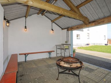 A covered outdoor seating area with benches a metal fire pit and a sink at Bryn Afon Farm in Llanrug