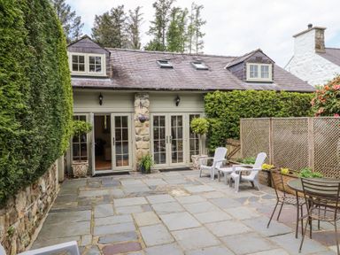 A stone patio with outdoor chairs and tables outside a cottage with dormer windows at Garden Cottage in Garndolbenmaen near Tremadog