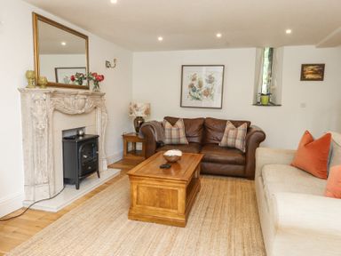 A living room with a brown leather sofa, beige sofa, wooden coffee table, decorative fireplace, and floral artwork at Garden Cottage in Garndolbenmaen near Tremadog