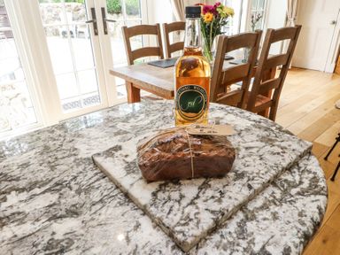 A kitchen with a marble countertop a loaf of bread wrapped in plastic and a bottle on the counter and a wooden dining table with chairs and flowers at Garden Cottage in Garndolbenmaen near Tremadog