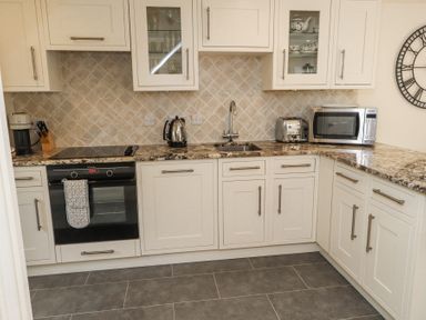 A kitchen with white cabinets a countertop oven kettle toaster microwave and sink at Garden Cottage in Garndolbenmaen near Tremadog