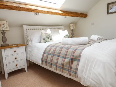 A bedroom with a bed with white sheets and plaid blanket two bedside tables with lamps under a wooden beam at Garden Cottage in Garndolbenmaen near Tremadog