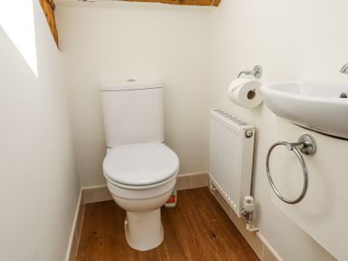 A small bathroom with a toilet, wall-mounted sink, radiator, and toilet paper holder at Garden Cottage in Garndolbenmaen near Tremadog