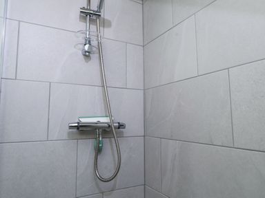 A shower area with a wall-mounted showerhead and control unit in a tiled bathroom at Garden Cottage Garndolbenmaen near Tremadog
