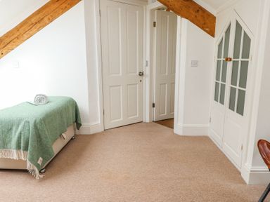 A bedroom with a single bed covered by a green blanket and a rolled towel two closed doors a built in white cabinet with glass panels wooden ceiling beams and beige carpet at Garden Cottage in Garndolbenmaen near Tremadog