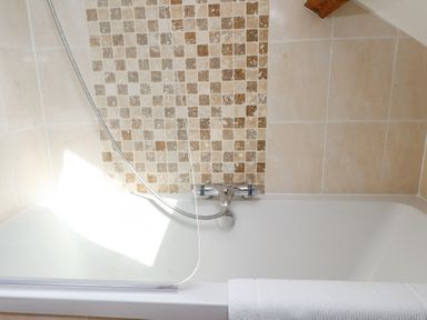 A bathtub with a shower attachment and tiled walls with beige and brown square patterns at Garden Cottage in Garndolbenmaen near Tremadog
