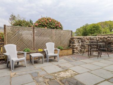 An outdoor patio with two white plastic chairs and a small table next to a wooden lattice fence and a round metal table with four chairs near a stone wall at Garden Cottage in Garndolbenmaen near Tremadog