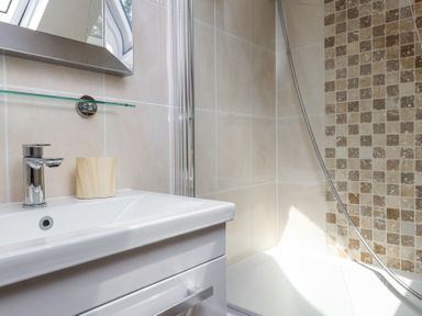 A bathroom sink with a faucet and a wooden cup next to a bathtub with tiled walls at Garden Cottage in Garndolbenmaen near Tremadog