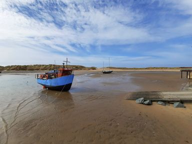 A blue and red boat and a sailboat on a sandy shore with a wooden ramp and rocks at Sapphire Suite in Barmouth