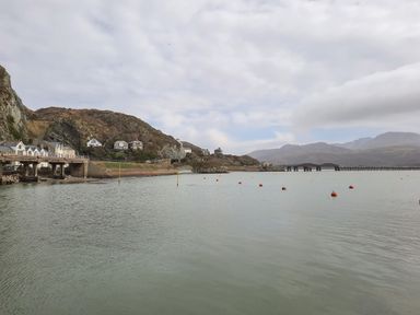 A body of water with orange buoys near houses on rocky hills and a long bridge in the background at Sapphire Suite in Barmouth