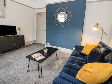 A living room with a blue sofa yellow cushions black coffee table and a wall-mounted mirror at Sapphire Suite in Barmouth
