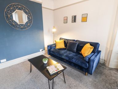 A living room with a blue sofa with cushions and a black coffee table with a plant and book at Sapphire Suite in Barmouth