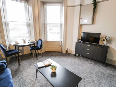 A living room with two blue chairs at a small round table and a black cabinet with a TV in Sapphire Suite in Barmouth