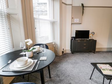 A dining table set with plates bowls and glasses next to a window and a television on a cabinet in a room at Sapphire Suite in Barmouth