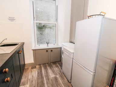A kitchen with a white refrigerator dishwasher gray cabinets and a window at Sapphire Suite in Barmouth