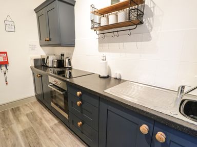 A kitchen with dark cabinets a countertop stove an oven a microwave toaster kettle and a sink at Sapphire Suite in Barmouth