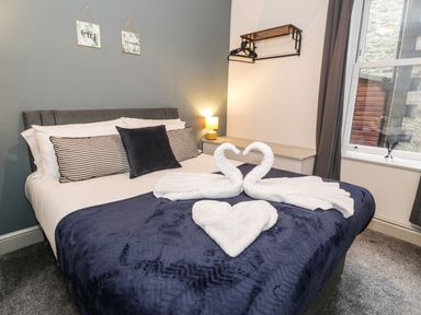 A bedroom with a double bed with folded towel swans and heart on a blue bedspread at Sapphire Suite in Barmouth