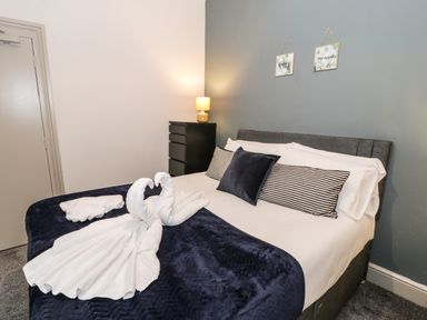 A bedroom with a bed decorated with towel swans a black chest of drawers and two wall signs at Sapphire Suite in Barmouth
