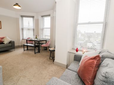 A living room with a gray sofa a dining table with pink chairs and large windows at Rose Suite in Barmouth