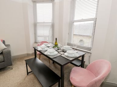 A dining table set with white plates and wine glasses near windows with blinds and pink chairs at Rose Suite in Barmouth