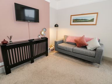 A living room with a wall mounted television above a black radiator cover and a gray sofa with cushions and a blanket at Rose Suite in Barmouth