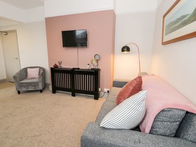 A living room with a gray sofa, cushions, a gray armchair, a wall-mounted TV, and a black cabinet at Rose Suite in Barmouth