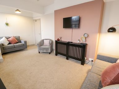 A living room with two grey sofas a grey armchair a wall-mounted TV and a radiator cover with decorations at Rose Suite in Barmouth
